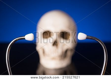 Stethoscope i focus and blurry skull isolated on black blue background