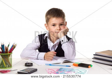 Cute intelligent pupil sitting at the desk with hand under the chin surrounded with stationery.