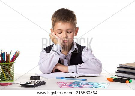 Cute bored pupil sitting with lowered eyes at the desk with hand under the chin surrounded with stationery.