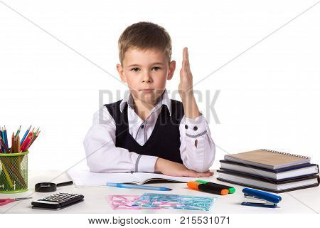 Humble excellent pupil with hand up sitting at the table on the white background.