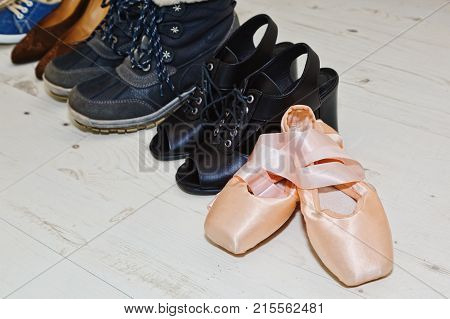 Collection of different female shoes - winter boots summer ankle boots sneakers and other a nd a pair of pink classic ballet dancing shoes with ribbons in the foreground. Selective focus.