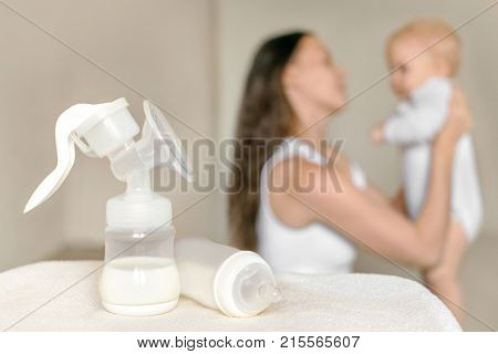 Manual breast pump and bottle with breast milk on the background of mother holding baby in her hands. Maternity and baby care.