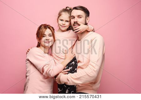 Happy young family with one little daughter posing together on pink studio background