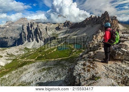 Hiker woman with backpack and mountain equipment, looking at view the Piani alpine glacier lakes, Dolomites, Italy, Europe
