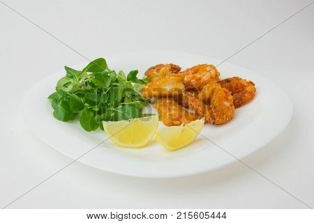 Fried shrimps on a plate. Prawns fried in breading on a white plate with salad and lemon.