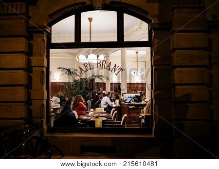 STRASBOURG FRANCE - NOV 21 2017: Tourists and locals drinking a warm coffee or tea inside the Brant Cafe in Strasbourg - view from the street at night