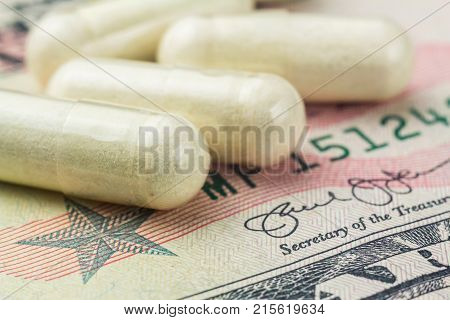 White capsules of glucosamine chondroitin healthy supplement pills on dollar banknote macro image.