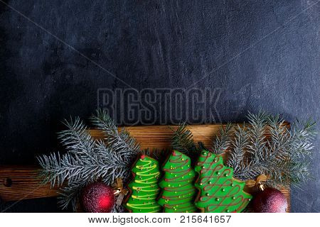 Chipboard with cookies in the form of fir-trees and twigs of spruce with toys lies horizontally down on a stone background