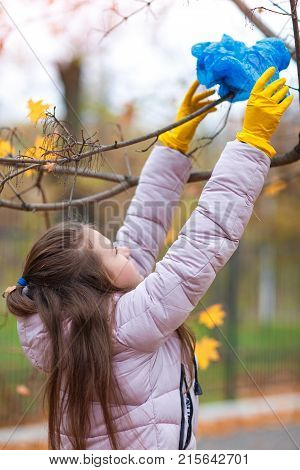 A girl in yellow, rubber gloves, reaches for a branch on a tree to take off the package, which is stuck there.