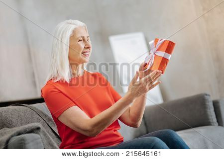 Birthday present. Positive pleasant elderly woman looking at the gift box and smiling while preparing a birthday present