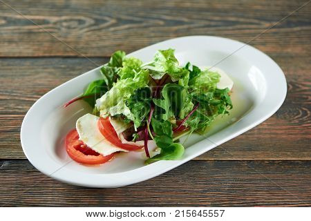 Close up horizontal shot of a plate with caprese Italian traditional salad on a wooden table at the restaurant tomatoes mozarella rucola greend delicious vegan healthy vegetables.