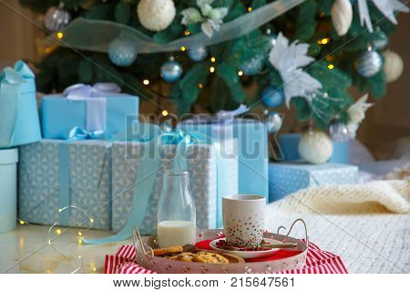 A traditional treat Christmas cookies and a glass of milk for Santa on white tray. New year's concept. Blue gift boxes