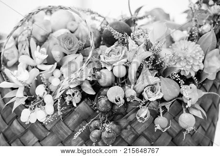beautiful decoration floral composition or bouquet of seasonal fruits grapes dogrose rosehip and physalis or winter cherry with many flowers orange violet and green color in straw basket