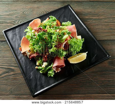 Top view shot of a black plate with salad and ham on a wooden table at the restaurant sauce mustard spicy delicious healthy food menu gourmet cooking cusine recipe.