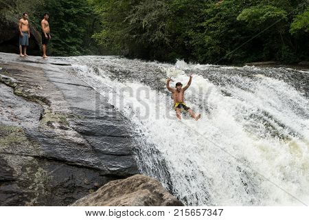 CASHIERS, NORTH CAROLINA - AUGUST 21, 2016: Young adult slides down rocks in Turtleback Falls in Gorges State Park near Cashiers in North Carolina, USA