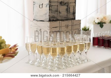 Welcome drinks stand with a lot of champagne glasses, fruits and juices on wedding and retro suitcase behind