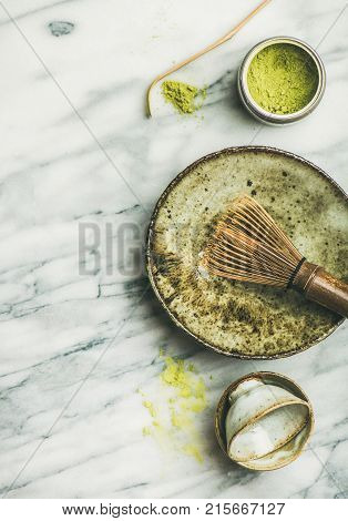 Flat-lay of Japanese tools and bowls for brewing matcha green tea. Matcha powder in tin can, Chashaku spoon, Chasen bamboo whisk, Chawan bowl, cups over grey marble background, top view, copy space