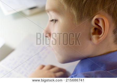 Close-up of boy hand with pencil writing english words by hand on traditional white notepad paper. Boy writes a letter to a friend