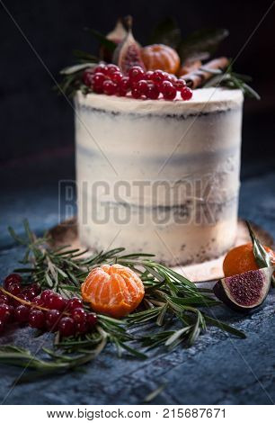 Close-up of white christmas cake decorated with red berries tangerin figs and rosemary