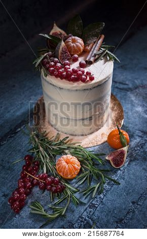 Angle shot of white christmas cake decorated with red berries tangerin figs cinnamon stick and rosemary
