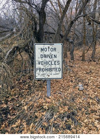 Motor Driven Vehicles Prohibited by order of the Sheriff sign with bullet holes, in forest trail on the Yellow Fork and Rose Canyon Trails in Oquirrh Mountains on the Wasatch Front in Salt Lake County Utah USA.