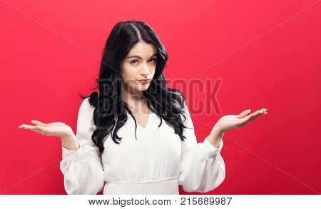 Young woman shrugging on a solid background
