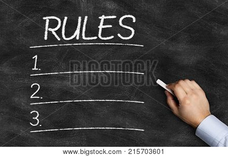 Rules List written on the blackboard with hand holding white chalk