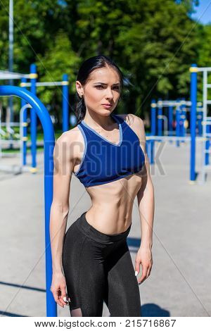 strong athletic teen in a bright blue sport bra and black leggings on the sport playground. Photo of an athlete girl with a beautiful sports body