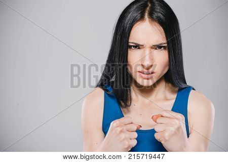 young teen with long brunette hair in blue dress making angry emotion in photostudio on gray background