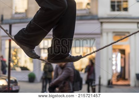 Tight rope walker's legs. Feet of balancing on rope in busy high street with passers by