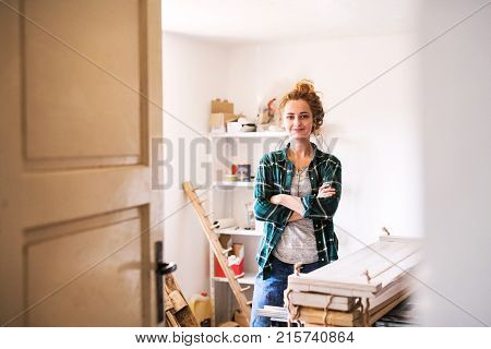 Small business of a young woman. Beautiful young woman worker in workroom. Female carpenter standing by her products, crossed arms.