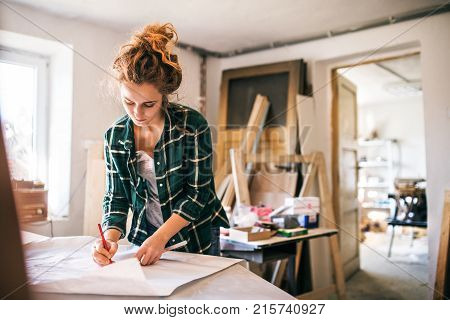 Small business of a young woman. Beautiful young woman worker in workroom. Female carpenter sketching a project.