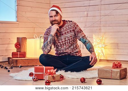 Redhead bearded male in Santa hat in a room with Christmas decoration.