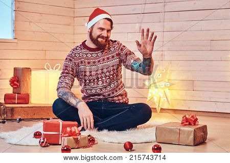 Redhead bearded male in Santa hat in a room with Christmas decoration.