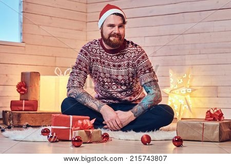 Redhead bearded male in Santa hat in a room with Christmas decoration.