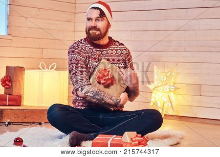 Redhead bearded male in Santa hat in a room with Christmas decoration.