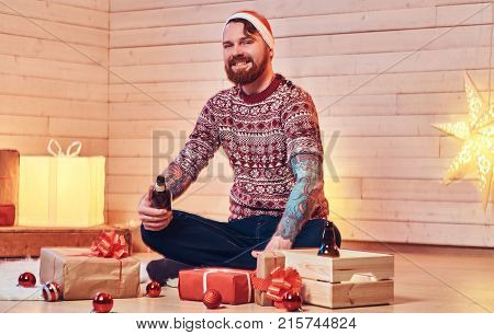 Redhead bearded male in Santa hat, drinks craft beer in a room with Christmas decoration.