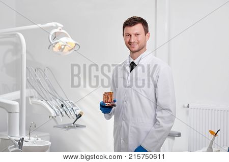 Portrait of a mature male dentist posing proudly at his clinic holding teeth model smiling to the camera copyspace profession occupation experience trust medicine health entistry oral examination.