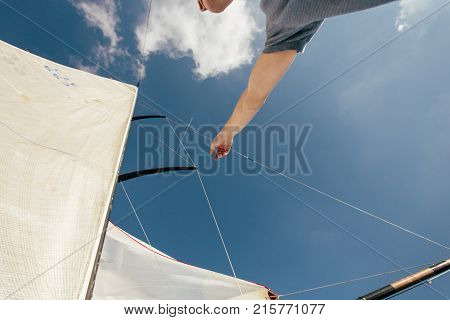 Professional sailor or yachtsman uses mast and forestay to put up spinnaker or mainsail on racing competition yacht or sailboat on warm summer day. Points on sail in blue sky