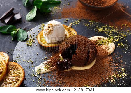Exquisite french dessert. Chocolate fondant, creme anglaise and vanilla ice cream, sprinkled with cocoa powder, served on round slate finely decorated with orange citron and pistachio crumble, closeup
