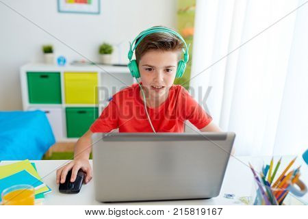 technology, gaming and people concept - boy in headphones playing video game on laptop computer at home