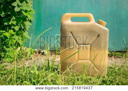 Plastic old vintage canister for liquid on the background of blue garage door and bright green grass. Concept of fuel for cars