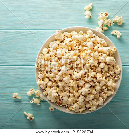 Cheddar cheese salted popcorn in a white bowl on light blue table overhead shot