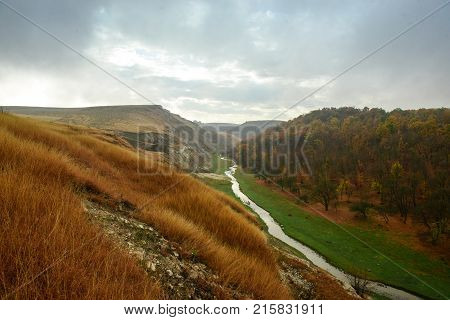 Beautiful landscape of the autumn forest in rainy day. Between the mountains a small river flows. Moldova, Edinet