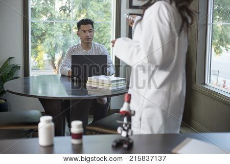 Female scientist in a lab coat researching with her male coed med school student in a campus laboratory. The woman is learning science and technology in medical industry.