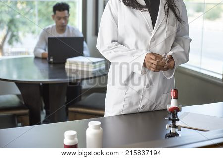 Female scientist in a lab coat researching with her male coed med school student in a campus laboratory. The woman is learning science and technology in medical industry.