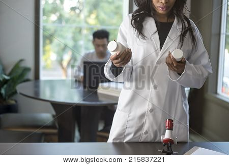 Female scientist in a lab coat researching with her male coed med school student in a campus laboratory. The woman is learning science and technology in medical industry.