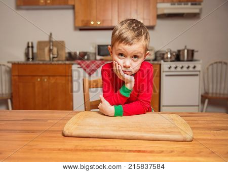 bored little boy sitting in the kitchen at the table. little kid is waiting