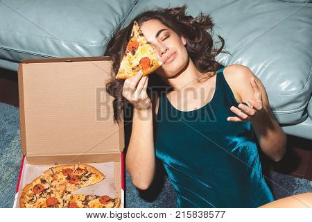 young cute woman lies with piece of pizza at home interior