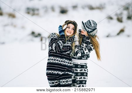 Couple of young woman. Girl wears warm hat girl closes friend's ears with her hands in mittens in cold winter